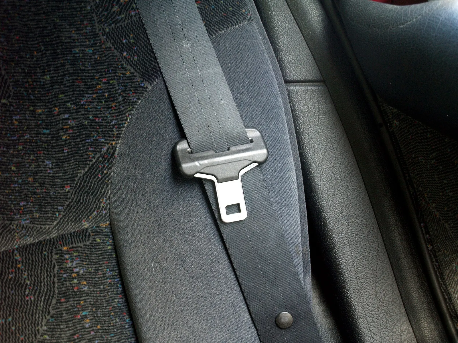 Close-up of a grey car seat belt and its metal buckle tongue.