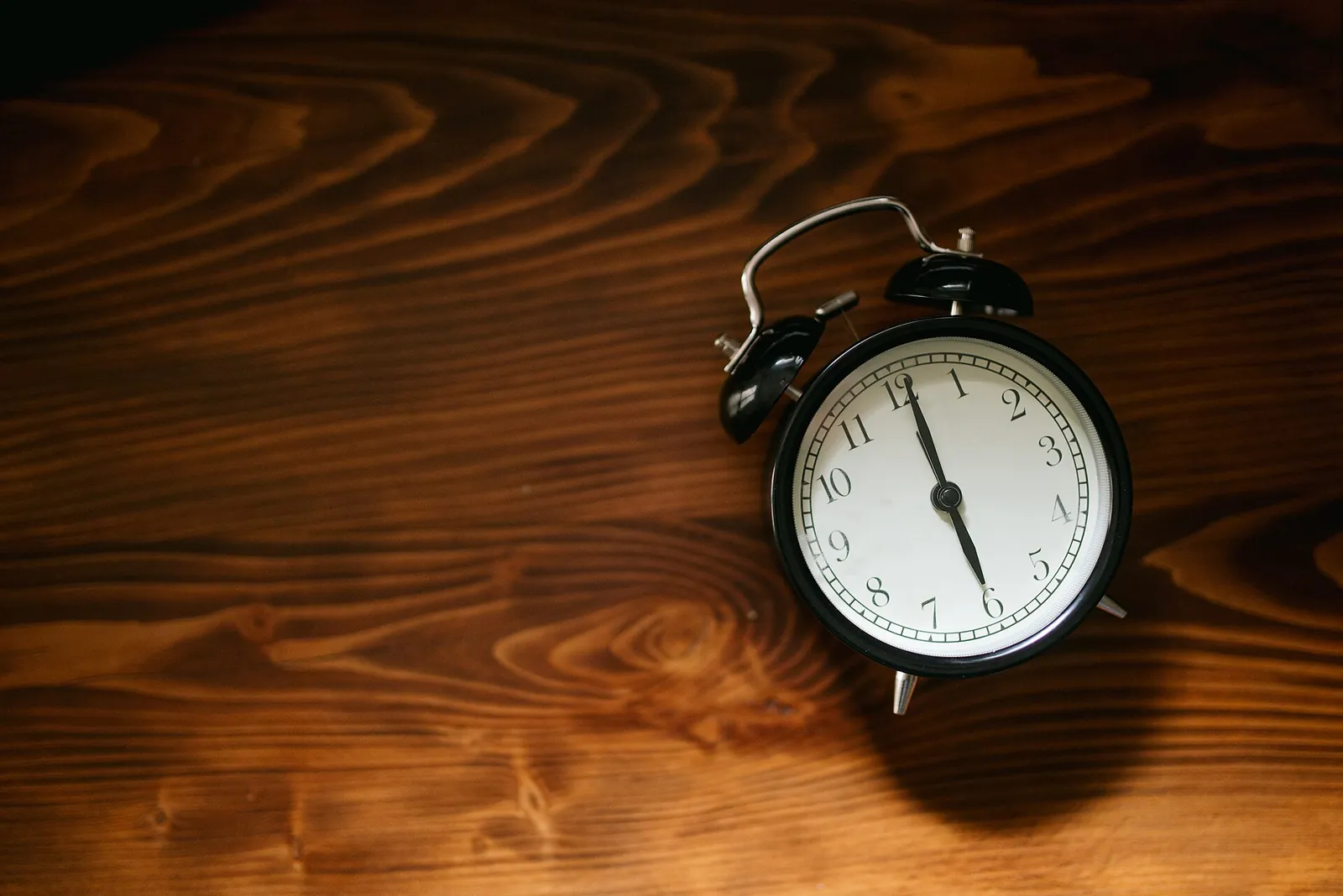 A black analogue alarm clock lying on a dark wooden surface.
