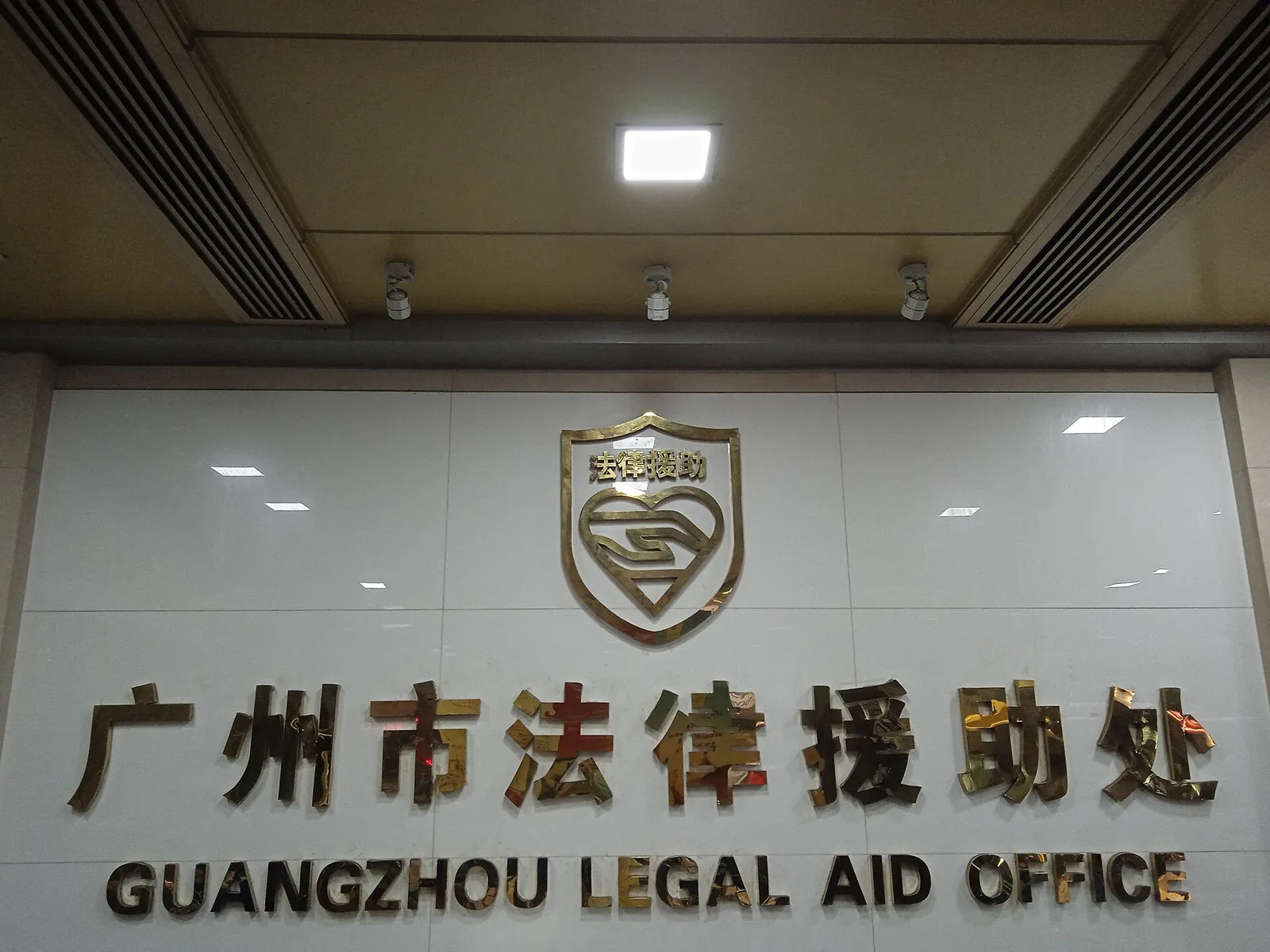The sign of the Guangzhou Legal Aid Office on a white wall.