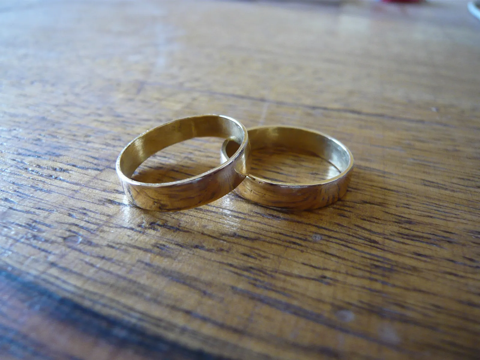 Two plain gold wedding rings lying on a wooden table.
