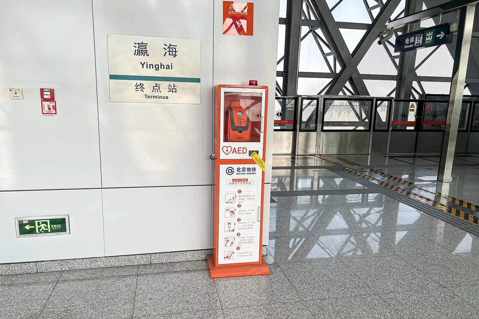 An orange public defibrillator (AED) cabinet on an empty Beijing Subway platform.