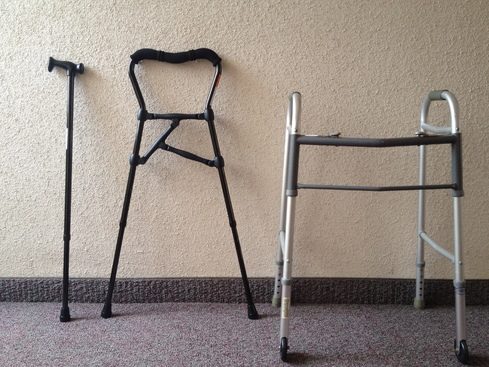 A walking cane, a cane-walker hybrid and a folding walker standing against a wall.
