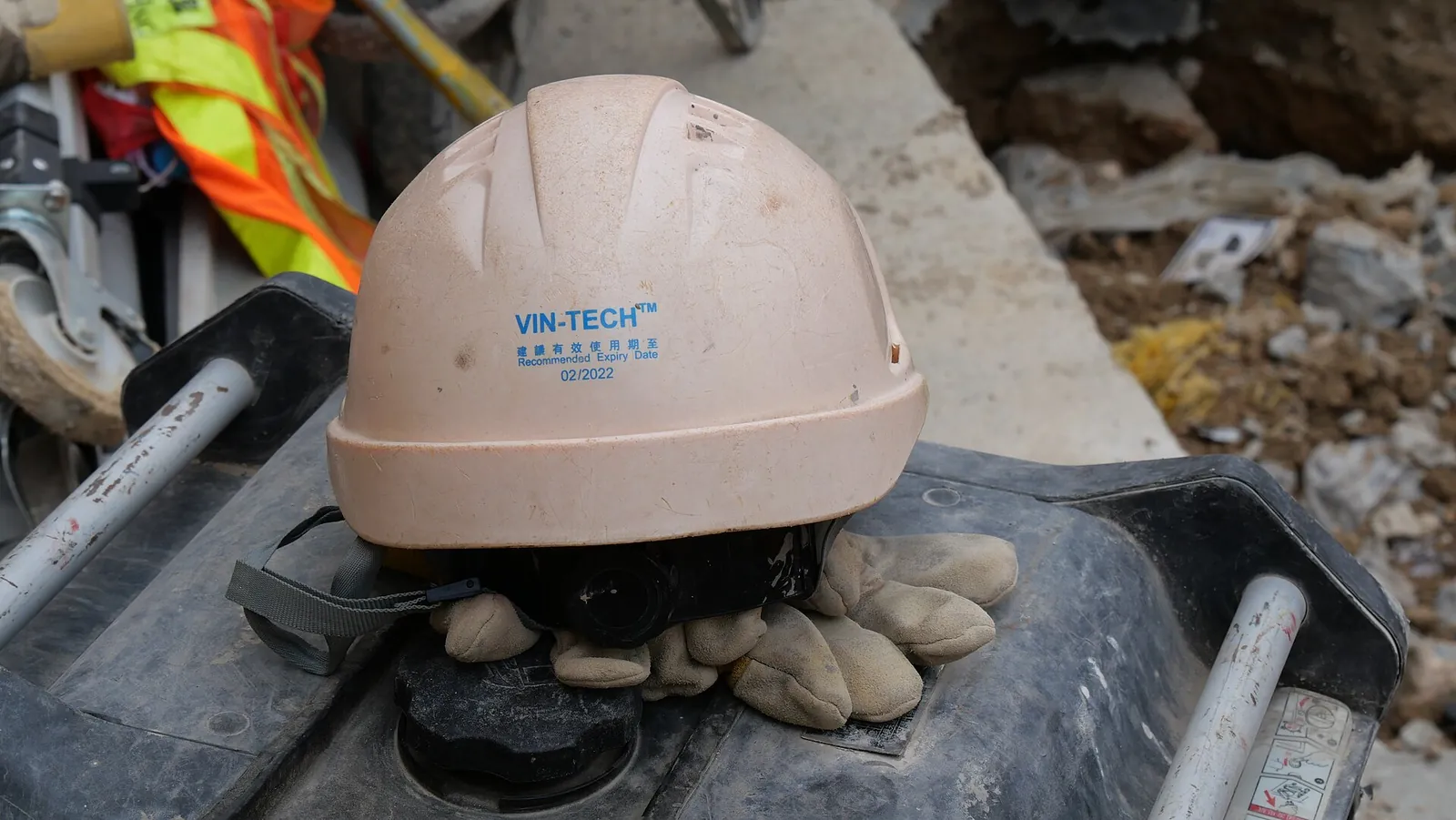 A white hard hat and a pair of work gloves resting on machinery.
