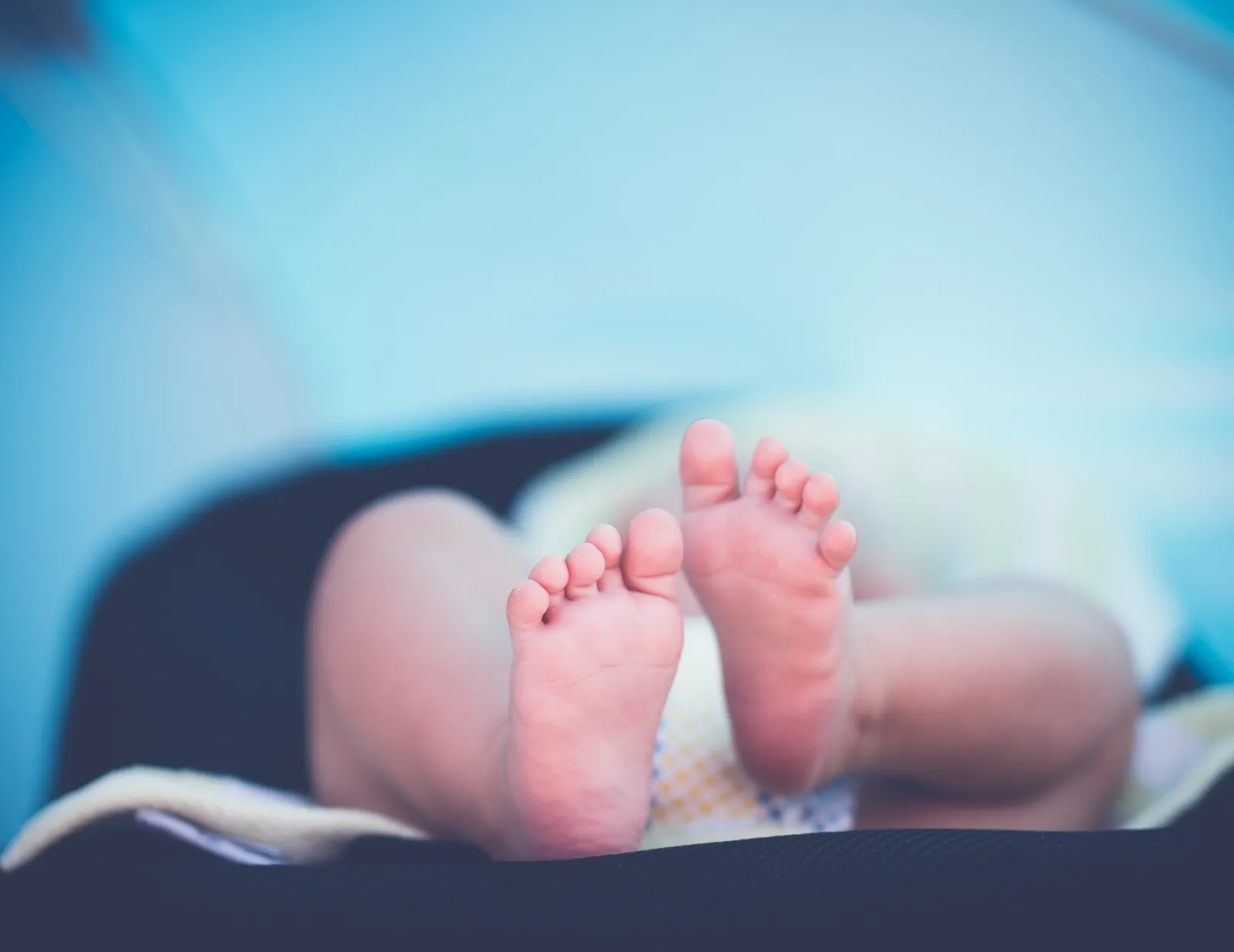 The bare feet of a newborn baby on a soft blanket.