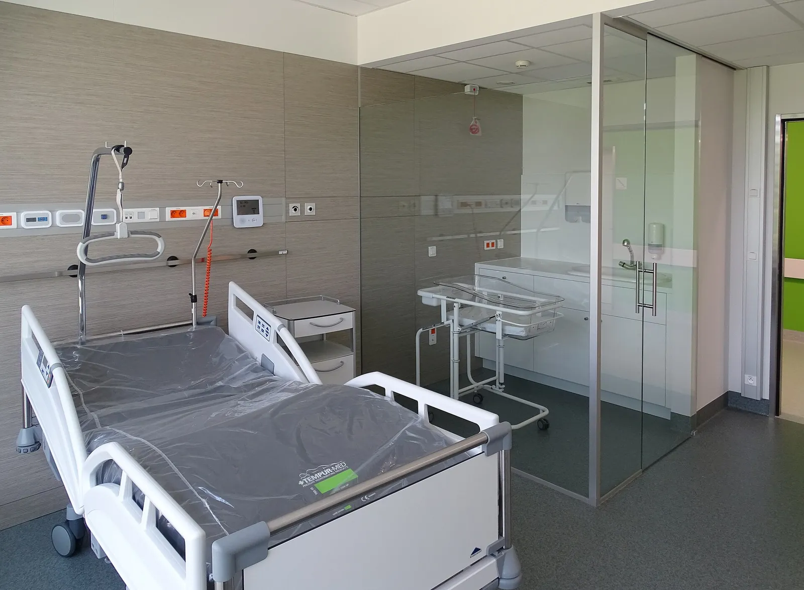 An empty hospital maternity room with an adjustable bed and a newborn bassinet.