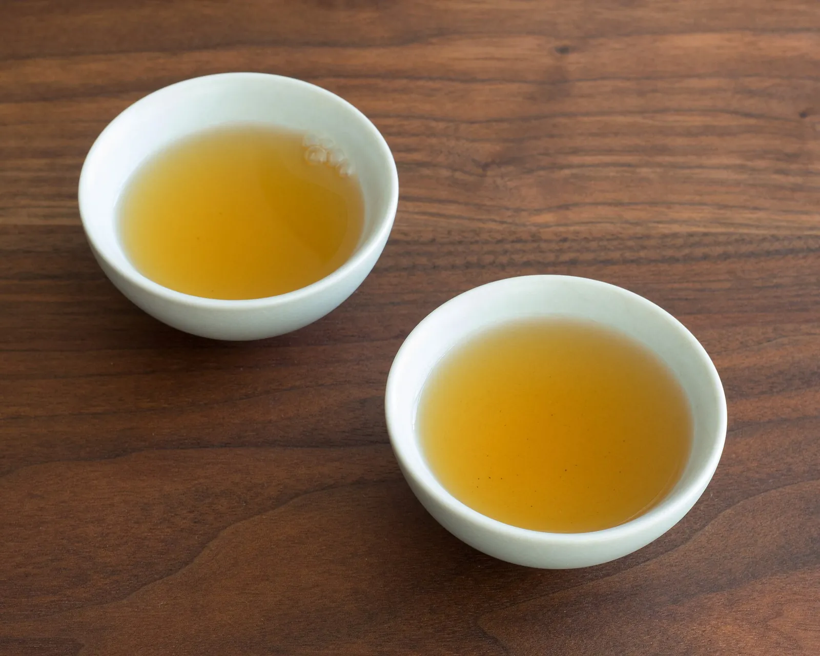 Two small cups of tea side by side on a wooden table.
