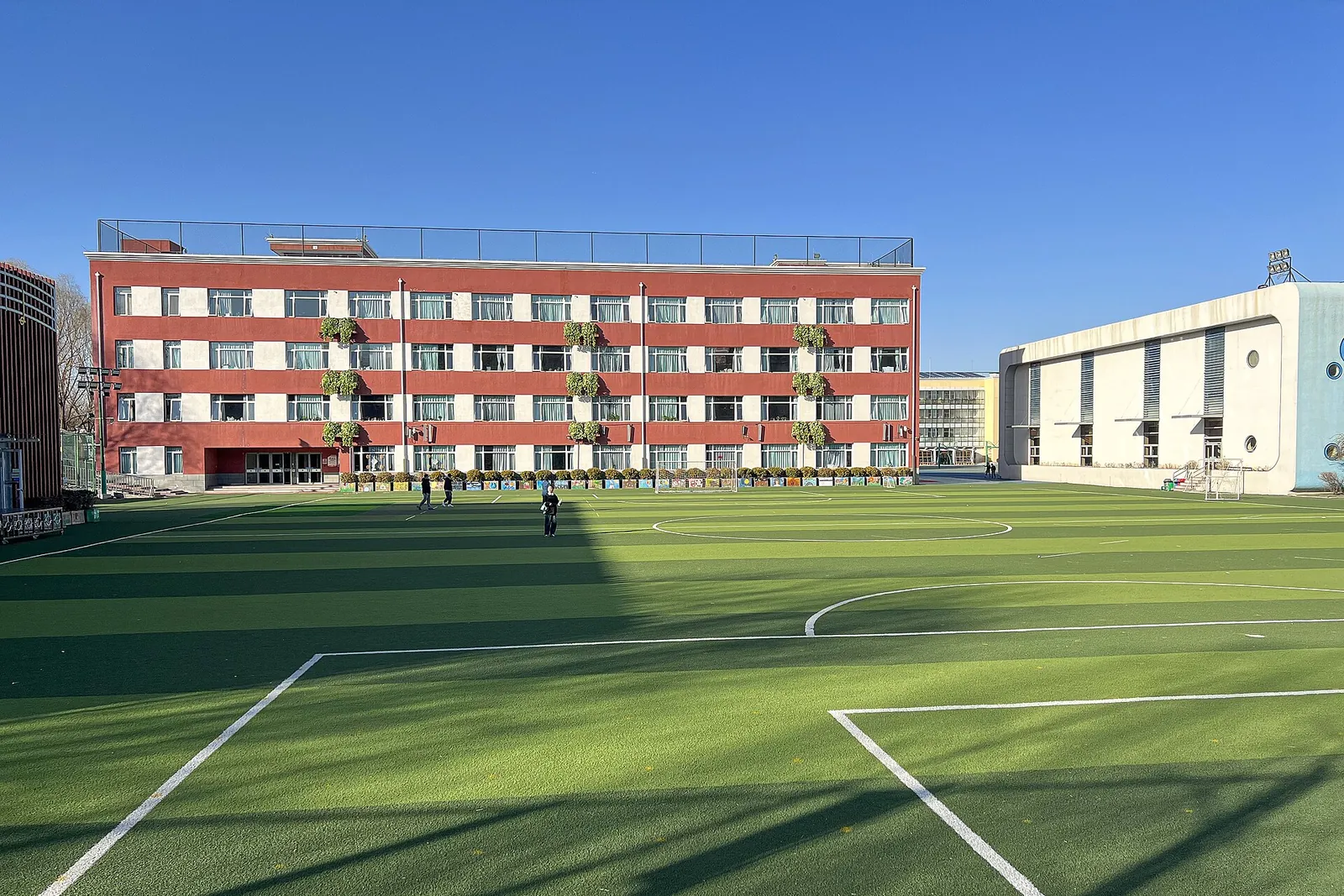 The sports field of a Beijing primary school in winter sunlight, with the school building behind it.